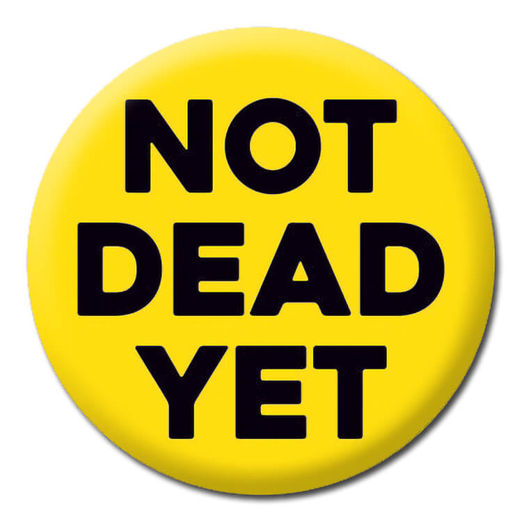 A bright yellow badge with bold square capital letters that read Not dead yet.
