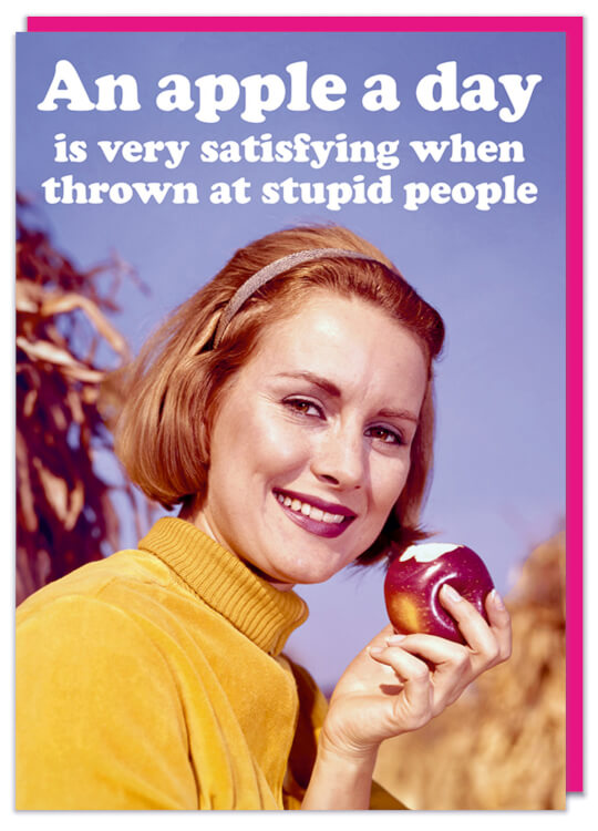 A greeting card with a smiling autumnal looking woman looking to camera and eating an apple.  White rounded text above her reads An apple a day is very satisfying when thrown at stupid people